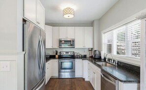 A kitchen with white cabinets, stainless steel appliances, a granite countertop, and a window with blinds. - The Lili Pad - Modern Lakefront Condo w/ Boat Slip and Breathtaking Views (LaFollette)