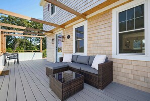 A covered outdoor seating area with a sofa and chairs, a glass-top coffee table, and a pergola structure. - Walk To The Beach, Rooftop Deck With Water Views (Bourne)