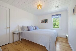 Une chambre à coucher comprenant un lit, une table de chevet, une fenêtre donnant sur un espace verdoyant et un luminaire au plafond.