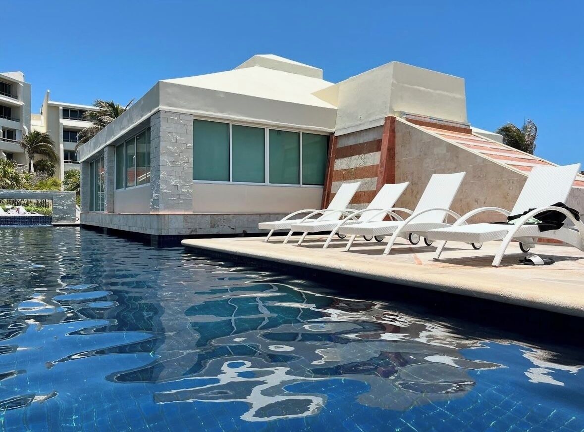 A swimming pool with lounge chairs and a building with large windows.