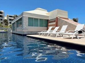A swimming pool with lounge chairs and a building with large windows. - Eight Bedroom Beachfront Villa - Private Heated Pool & Beach Access (Cancun)