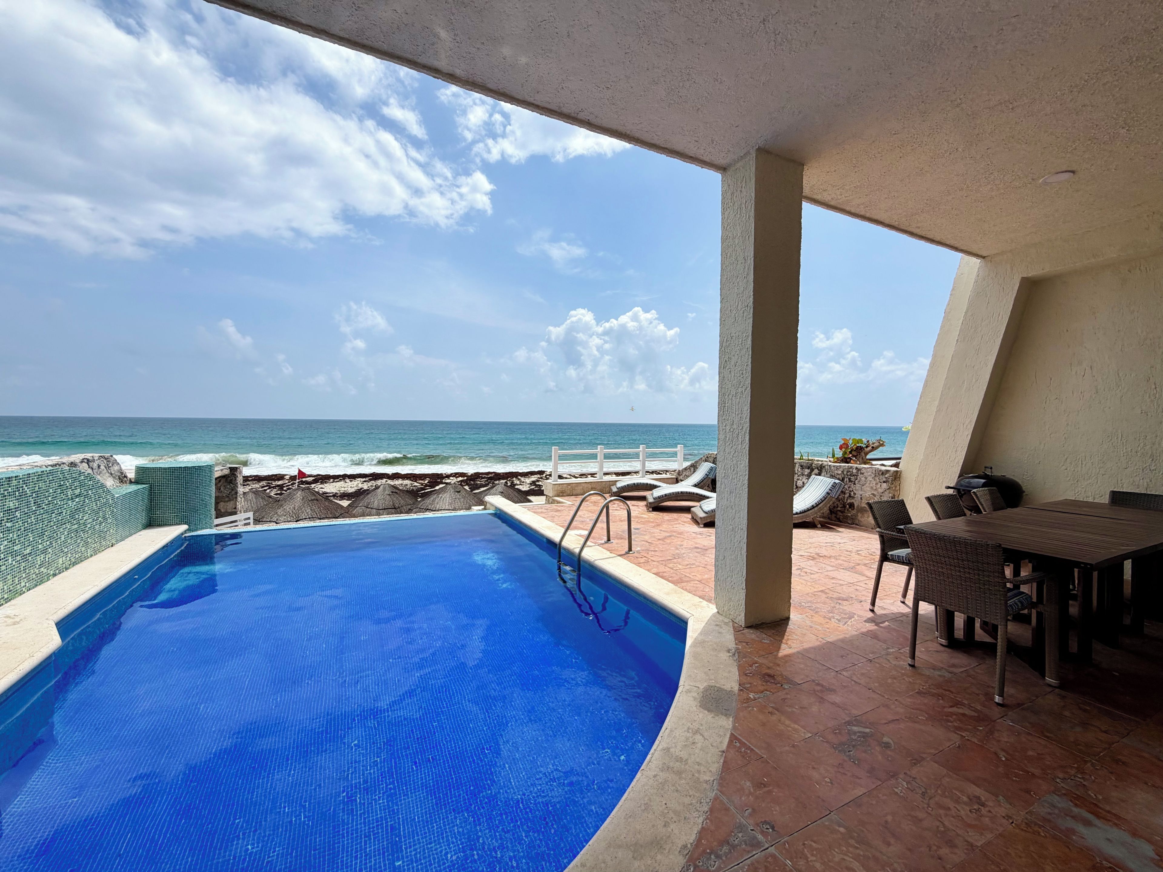 A pool with a view of the ocean, a barbecue grill, and outdoor seating.