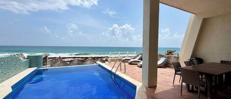 A pool with a view of the ocean, a barbecue grill, and outdoor seating.