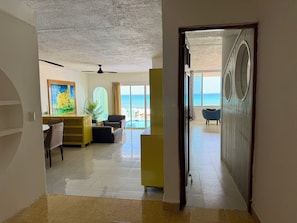 A hotel room with a view of the ocean, a ceiling fan, and a dining area with a table and chairs.