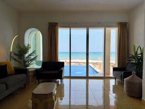 A modern living room with a view of the beach, a pool, and a sliding glass door.