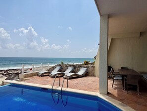 A pool area with lounge chairs and a view of the ocean.