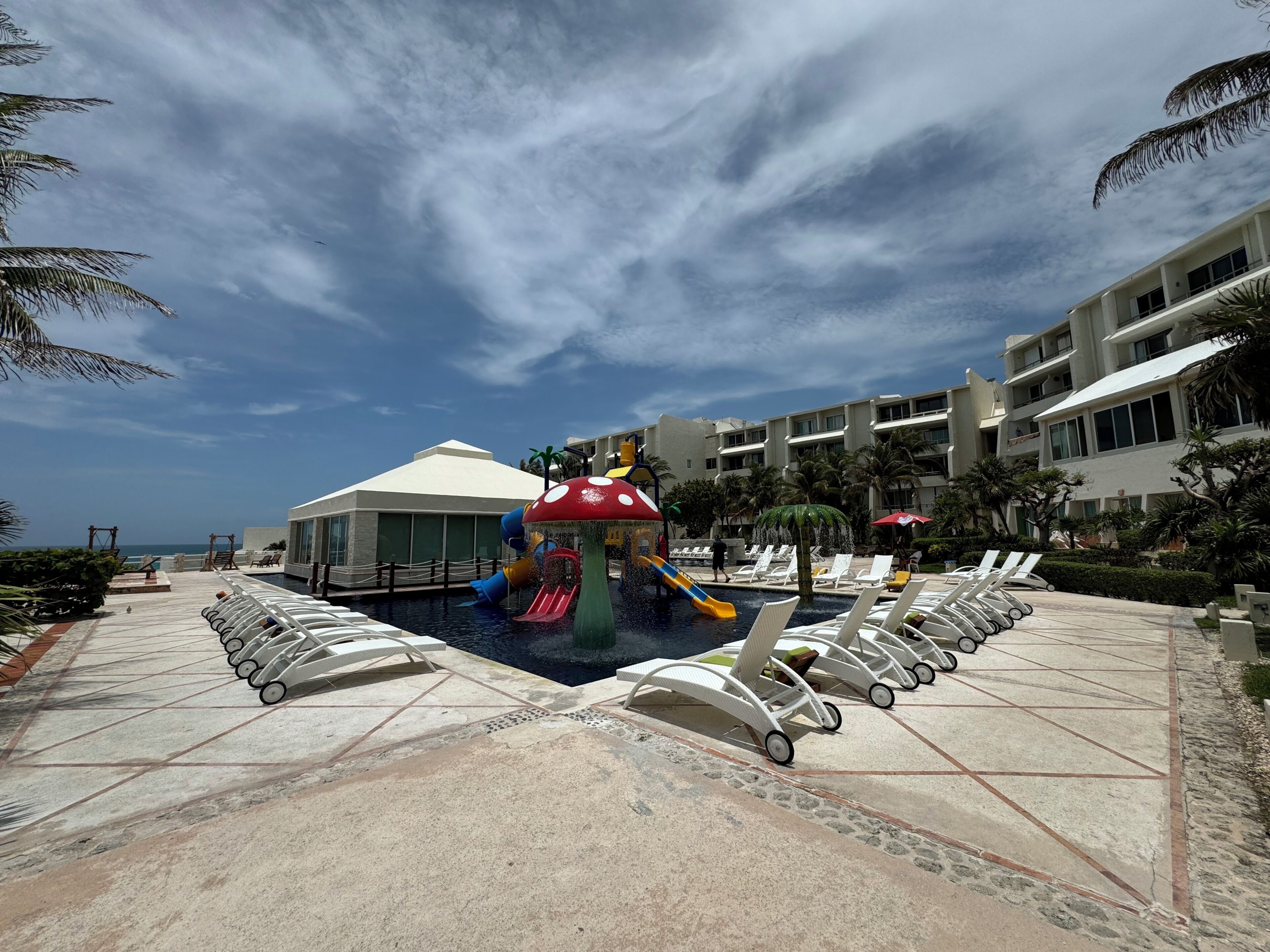 Uma área de piscina em resort com um toboágua, espreguiçadeiras e um edifício ao fundo.