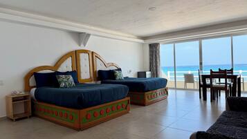 Quarto de hotel com duas camas, uma mesa de jantar e vista para o oceano.