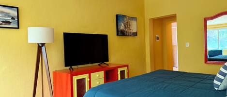 A hotel room with a bed, a flat-screen TV, a lamp, and a painting on the wall.
