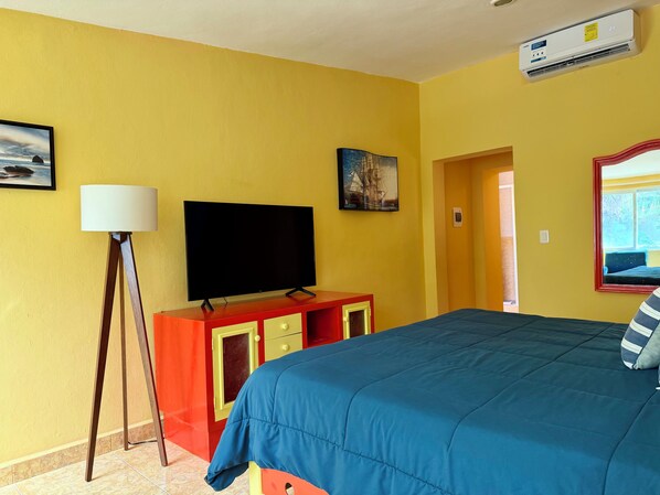 A hotel room with a bed, a flat-screen TV, a lamp, and a painting on the wall.