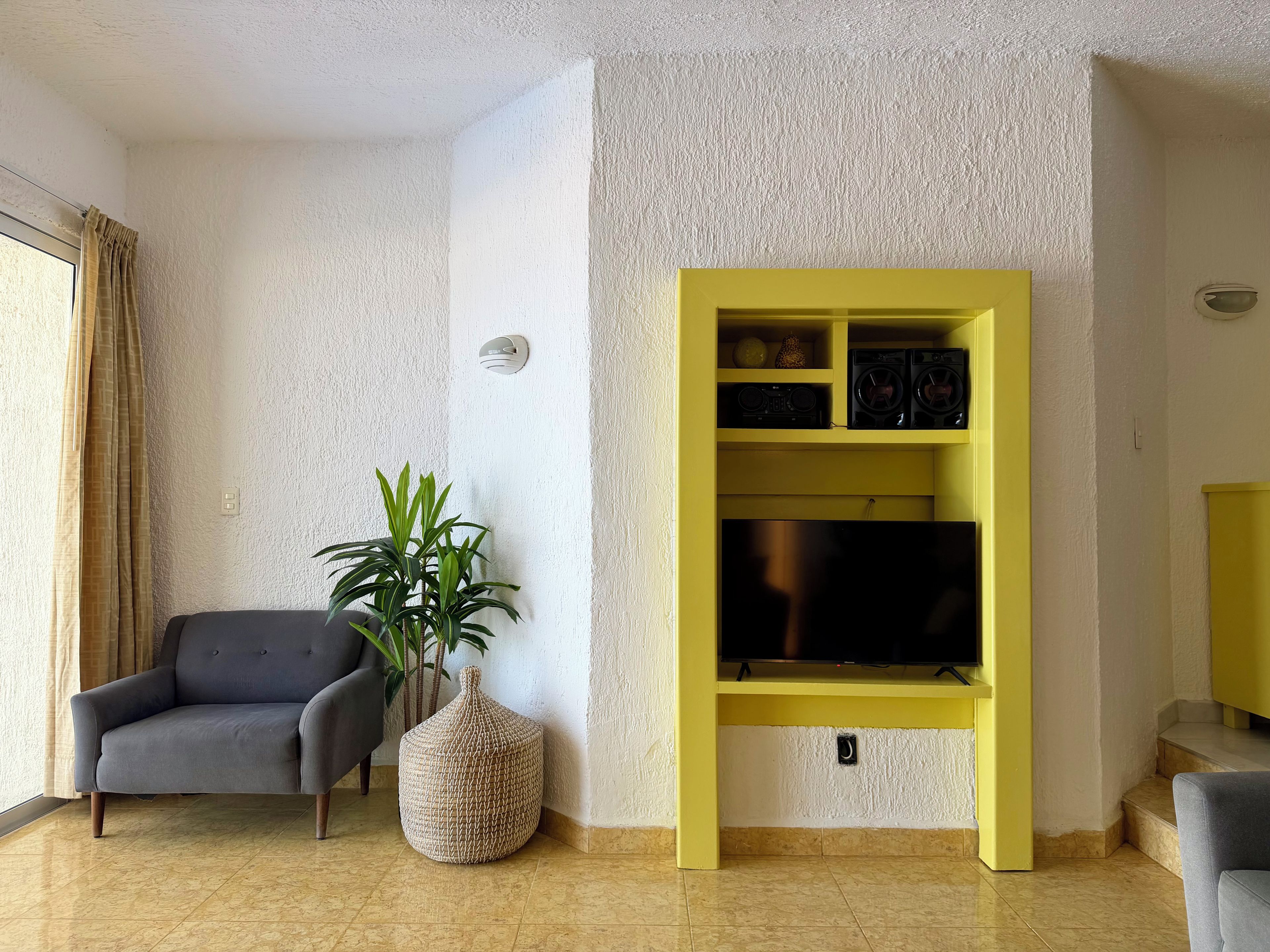 A living room with a sofa, a potted plant, a yellow entertainment unit, and a flat-screen TV.