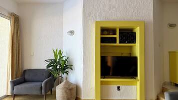 A living room with a sofa, a potted plant, a yellow entertainment unit, and a flat-screen TV.