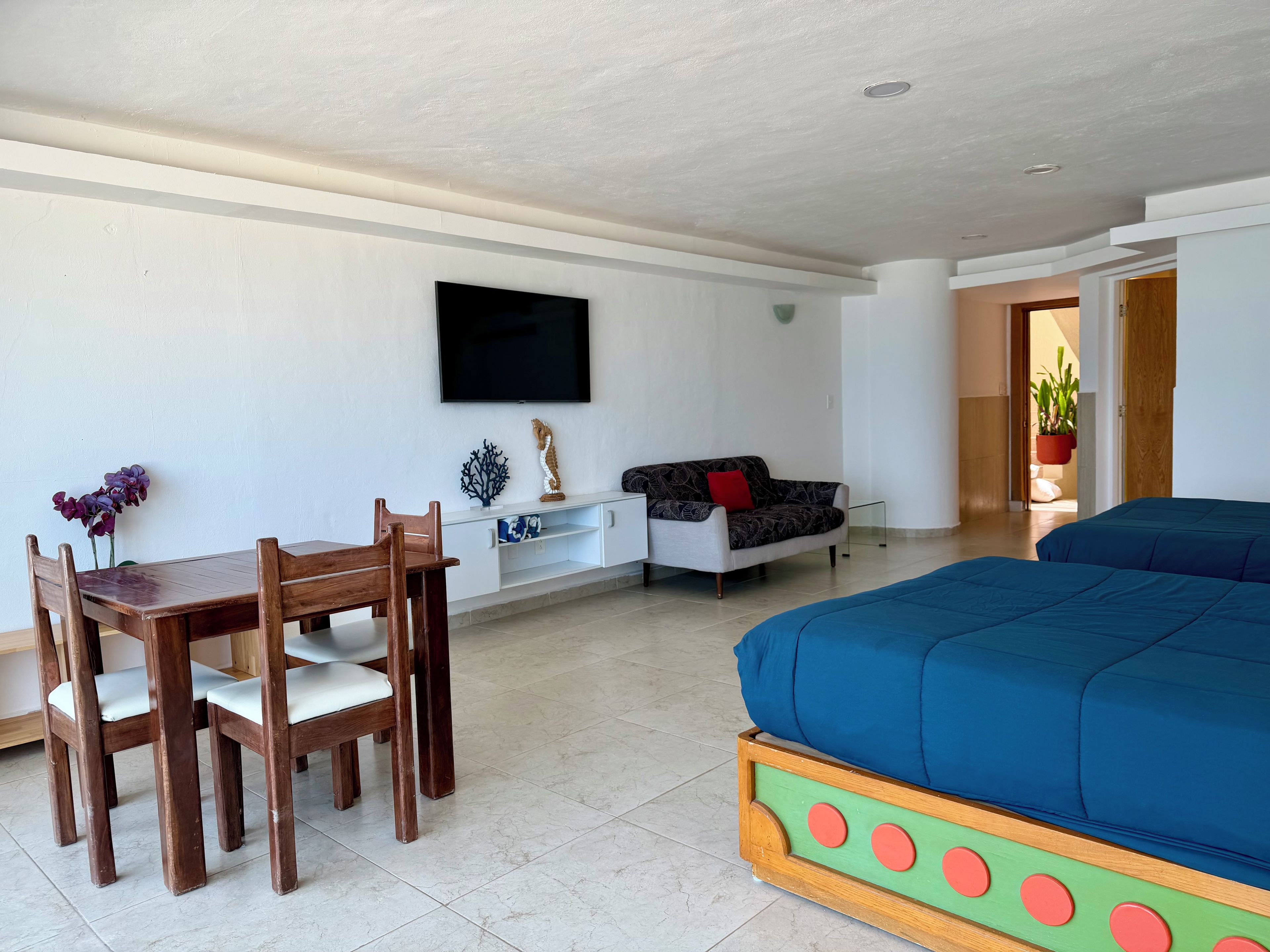 Ein Zimmer mit einem Bett, einem Schlafsofa, einem Fernseher, einem Esstisch mit Stühlen und einer Topfpflanze.