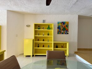 A room with a glass table, yellow shelving unit, and a painting on the wall.