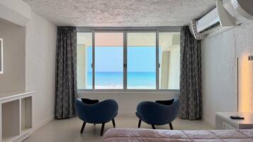 A bedroom with a large bed, two chairs, a TV, and a view of the sea.