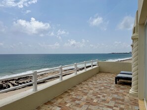 A balcony with a view of the sea, a tiled floor, and a white railing.