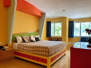 Ein Hotelzimmer mit Bett, Schreibtisch, Fenster mit Vorhängen und Blick auf Palmen.