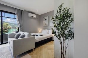 Ein modernes Schlafzimmer mit einem Bett, einem Sofa, einer Topfpflanze und Blick ins Freie.