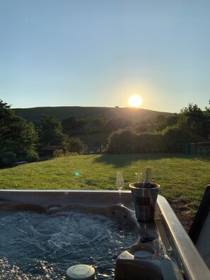 Ein Whirlpool mit Blick auf ein Wiesfeld und Hügel im Hintergrund.