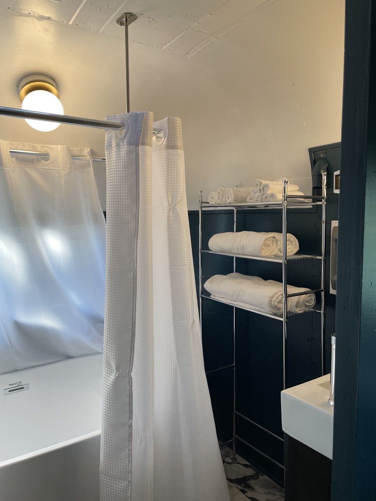 A bathroom with a shower curtain, a sink, and a towel rack with neatly folded towels.