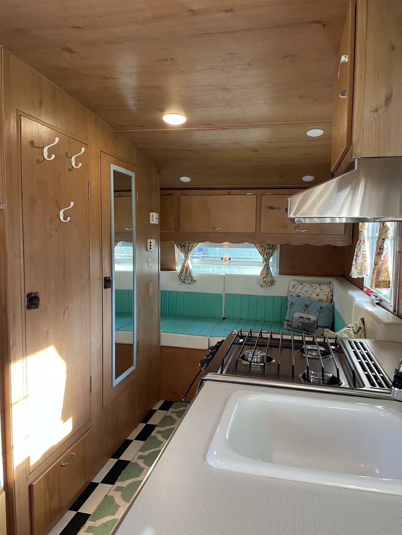 A compact RV kitchen with a gas stove, a sink, and a window seat with curtains.