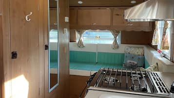 A compact RV kitchen with a gas stove, a sink, and a window seat with curtains.