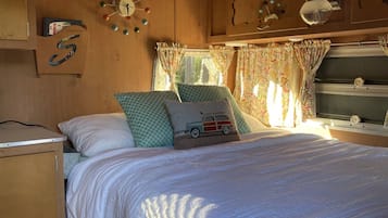 Un dormitorio de autocaravana acogedor con cama, almohadas, un reloj y una ventana con cortinas.