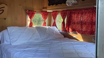 Ein Zimmer mit einem Einzelbett, Holzboden, einem Fenster mit roten Vorhängen und einer Wandleuchte.