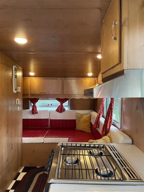 Una cocina compacta con estufa, armarios y una zona de estar con cojines rojos.