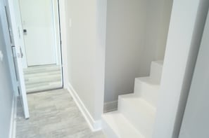 Un pasillo con suelo de madera y paredes blancas, que conduce a una puerta al final.
