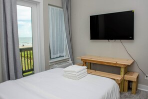 A bedroom with a bed, a wooden table, a TV mounted on the wall, and a window with a view of the beach. - Casa Dora Beach View Wave (Bolivar Peninsula)