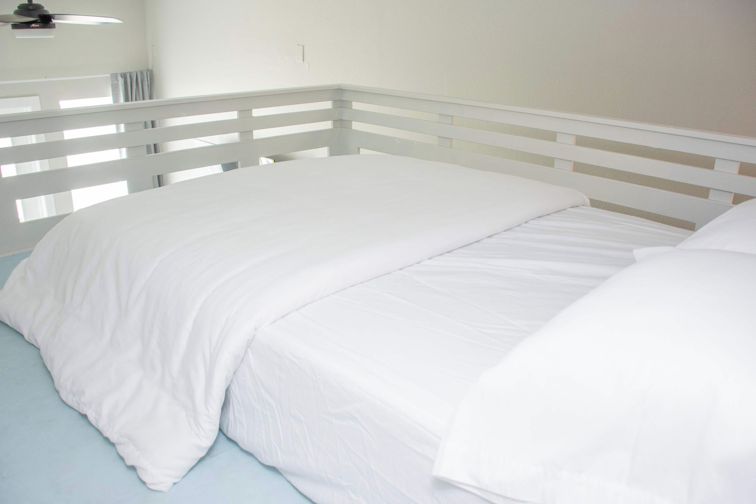 Una cama con ropa de cama blanca y cabecera blanca en una habitación con paredes blancas.