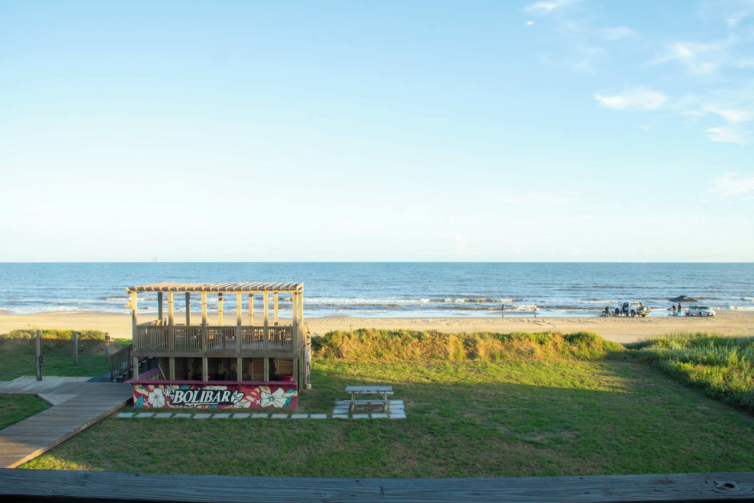 Een houten constructie aan het strand met een terras, een picknicktafel en een bord waarop 'BOLIBAR' staat.