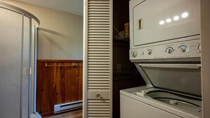 A laundry room with a dryer and washing machine, wooden closet doors, and a white wall. - Delightful Pinecone cottage in the charming village of Inlet (Inlet)