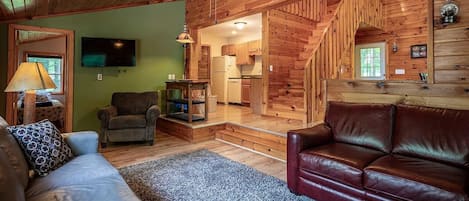 Un interior de madera con un sofá, una silla, un televisor y una escalera que lleva a una cocina.