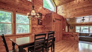 A wooden interior with a dining table and chairs, large windows, and a ceiling fan. - Delightful Pinecone cottage in the charming village of Inlet (Inlet)