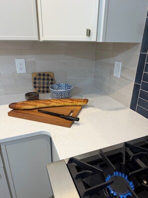 A kitchen with a white countertop, a wooden cutting board, a blue patterned bowl, and a loaf of bread. - Stay relax recharge, indulge in the perfect escape (Saugerties)