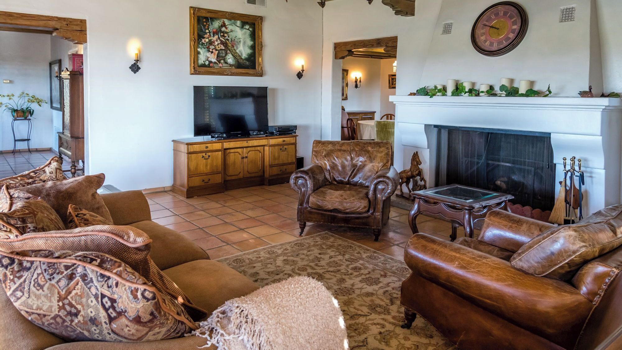 A living room with a fireplace, leather sofas, a television, and a decorative painting.