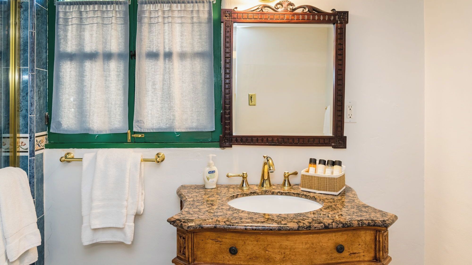 A bathroom with a granite countertop, a wooden vanity, a mirror, and a towel rack.