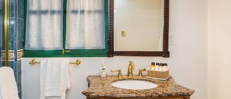 A bathroom with a granite countertop, a wooden vanity, a mirror, and a towel rack.