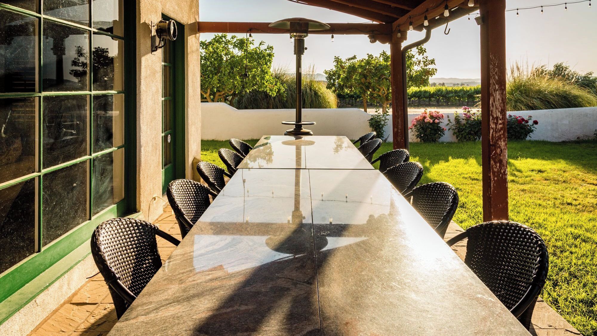 Une terrasse extérieure avec une longue table et des chaises, entourée de verdure et avec un vignoble en arrière-plan.