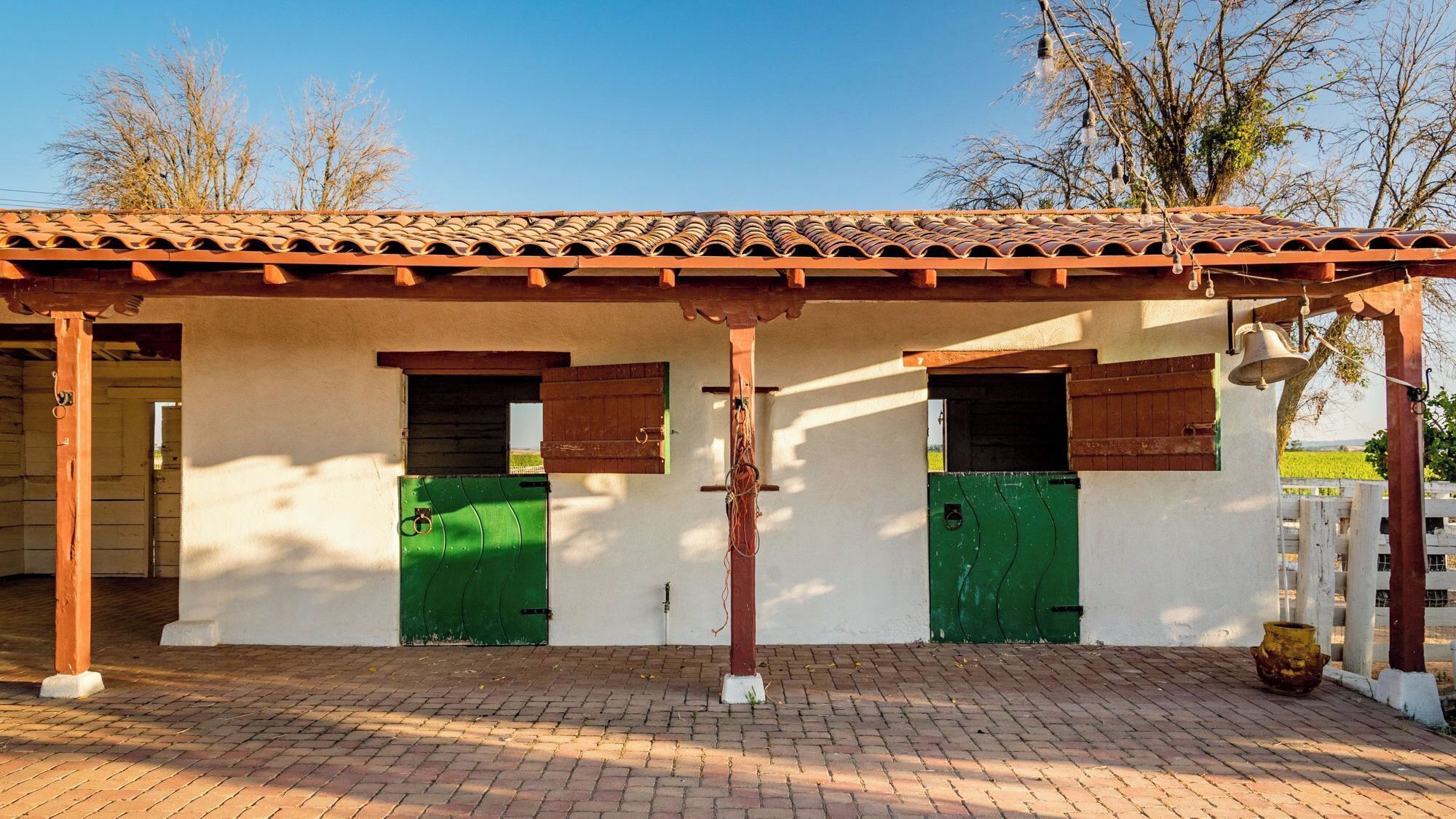 A building with a tiled roof, two green doors, and a bell.