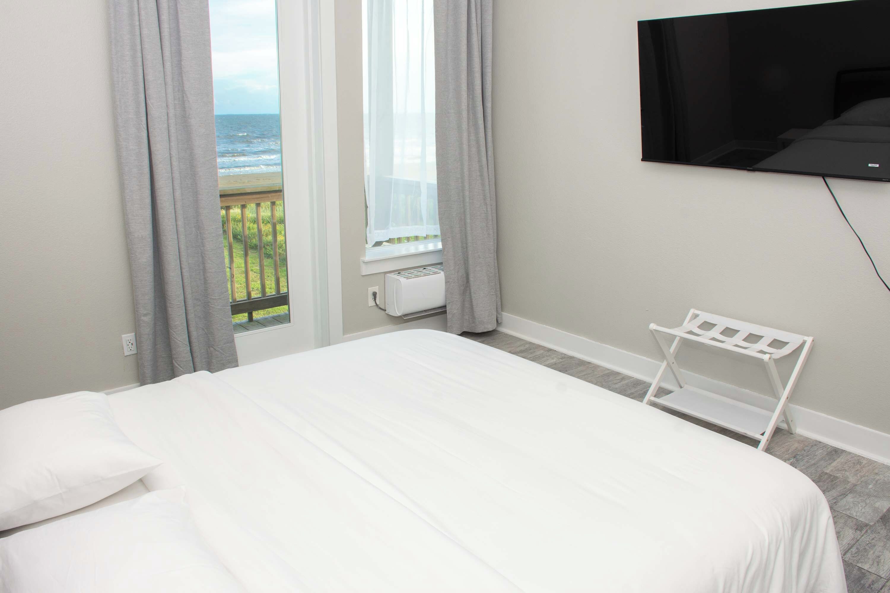 A hotel room with a bed, a TV mounted on the wall, and a window with a view of the sea.
