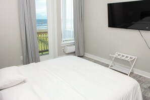 A hotel room with a bed, a TV mounted on the wall, and a window with a view of the sea. - Casa Dora Summer Breeze Beach View (Bolivar Peninsula)