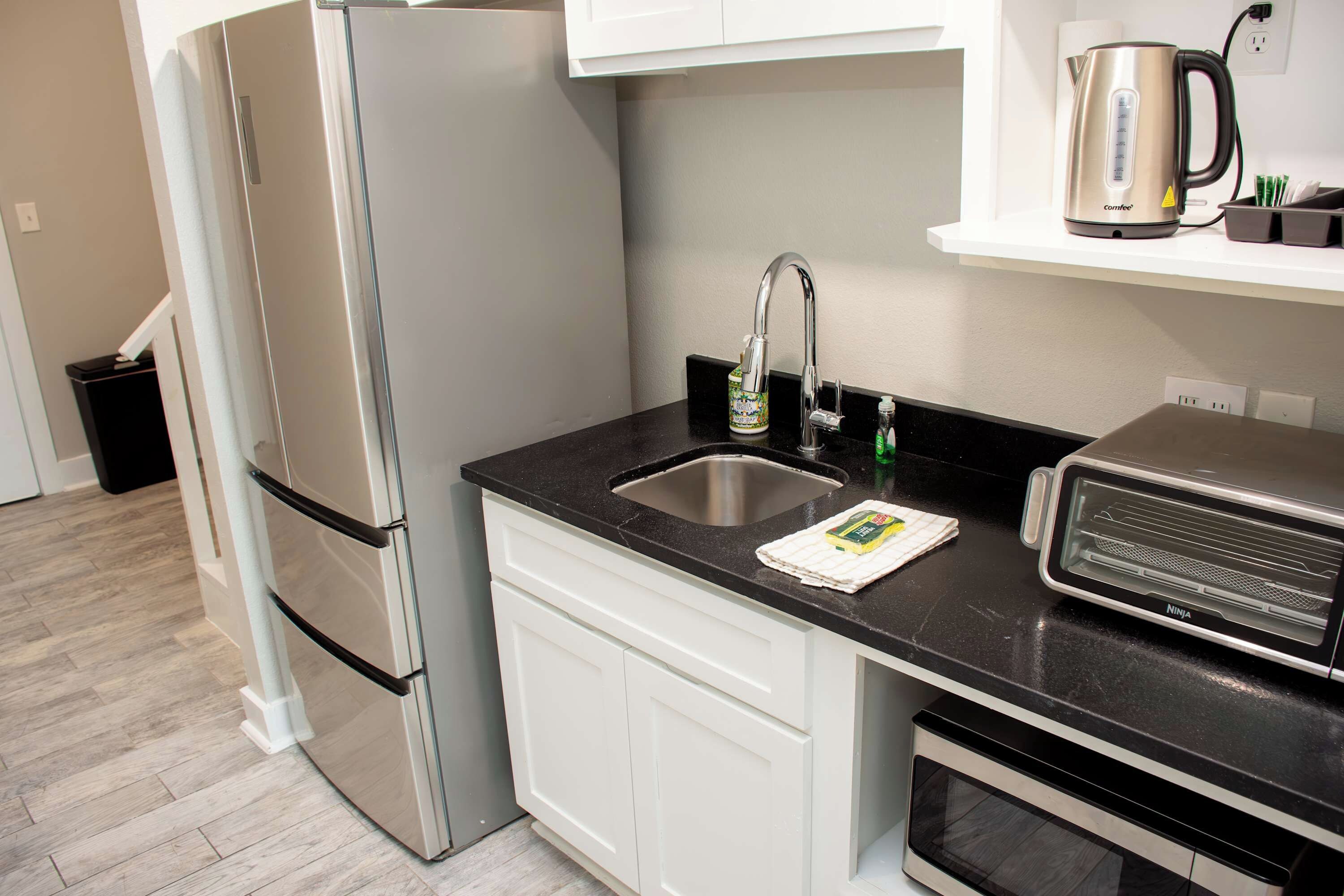 A modern kitchen with a stainless steel refrigerator, a built-in oven, a coffee maker, and a kettle on the countertop.
