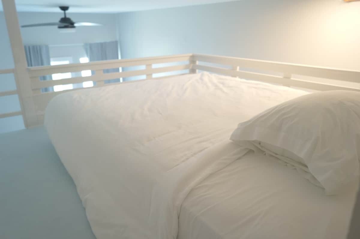 A bedroom with a white bed, a ceiling fan, and a white railing.