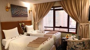 Habitación de hotel con dos camas, un ventanal grande, un adorno de pared y una pequeña zona de estar.