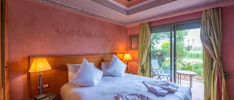 Habitación de hotel con una cama grande, una mesita de noche, una lámpara y vistas a un jardín a través de una puerta de cristal.