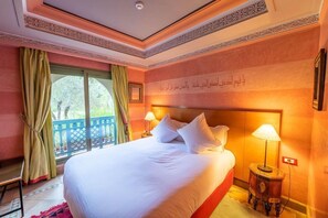 A hotel room with a large bed, two bedside lamps, a window with curtains, and a decorative wall with Arabic script. - Le Pavillon Du Golf (Marrakech)