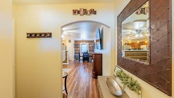 A hallway with a wooden floor, a coat rack, a mirror, and a sign that reads 'WELCOME'.